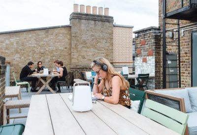 Rooftop terrace with wooden tables, seating, and views of surrounding brick buildings.
