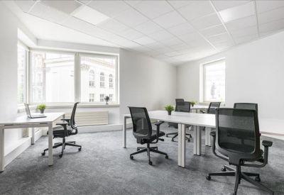 Bright open-plan office with white desks, black ergonomic chairs, and large windows.