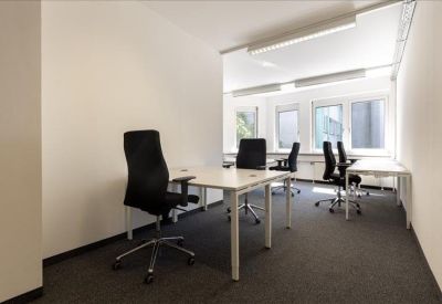 Bright four-person private office with white desks and black ergonomic chairs.