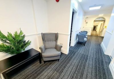 Hallway waiting area with a grey wingback chair and indoor plant.