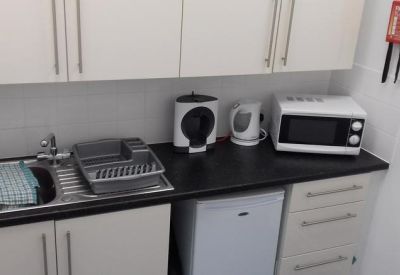 Small office kitchenette with white cabinets, microwave, and kettle.