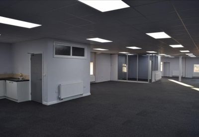 Large office area featuring a small kitchen unit and a glass-walled meeting room.