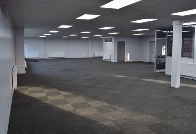 Spacious open-plan office space with grey carpeting and bright recessed ceiling lights.