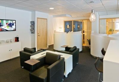 Breakout area with black armchairs, white tables, and a flat screen TV.