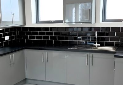 Modern communal kitchen with grey cabinetry, black tiled backsplash, and stainless steel sink.