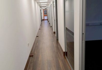 Bright hallway with wood-style flooring and glass-walled office entrances.