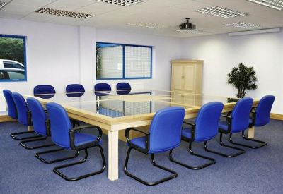 Formal boardroom with a large glass-topped table, blue chairs, and a potted plant.