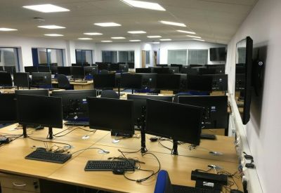 Spacious open-plan office with numerous workstations, monitors, and bright overhead lighting.