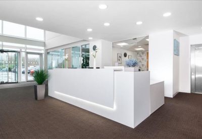 Minimalist white reception desk in a bright lobby with potted plants and brown carpeting.