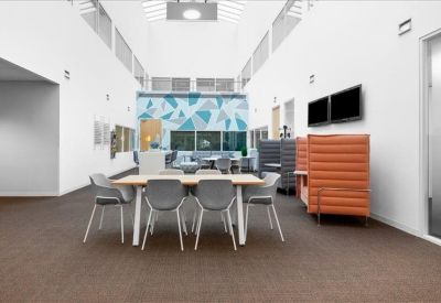 High-ceiling breakout area with a central dining table and orange privacy seating.