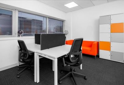 Modern private office with white desks, ergonomic chairs, and a bright orange sofa.
