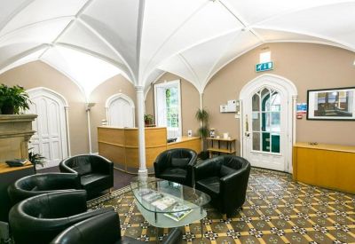 Reception area with a unique vaulted ceiling, decorative floor tiles, and black leather armchairs.