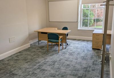 Bright private office featuring a corner desk, blue chairs, and a large sash window.