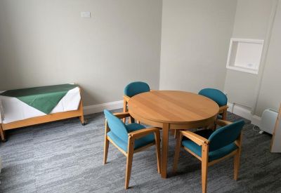 Small meeting room with a round wooden table, four blue chairs, and a grey carpet.