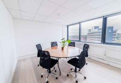 Sunlit meeting room with a round wooden table, black mesh chairs, and a small potted plant.