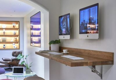 Coworking nook featuring a wall-mounted wooden desk, bar stools, and iMac workstations.