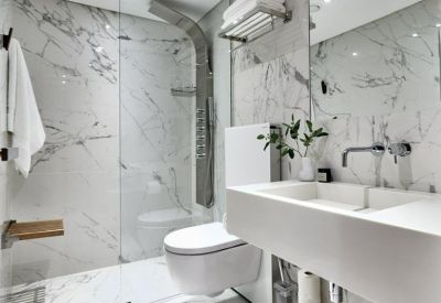 Modern white marble bathroom with a walk-in glass shower and floating sink.