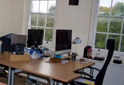 Well-lit office with multiple computer monitors, wooden desks, and large sash windows.
