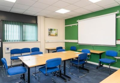 Bright meeting room featuring a green accent wall, blue chairs, and a large projection screen.