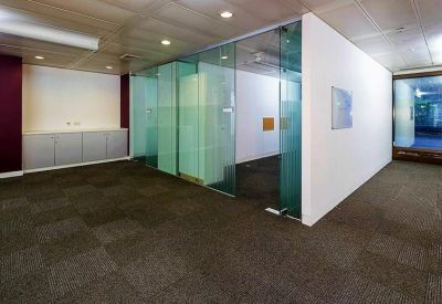 Empty office floor with dark carpeting and glass partitions under recessed lighting.