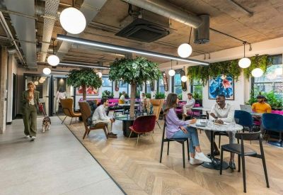 Spacious communal lounge with herringbone wood floors, indoor trees, and various seating areas.