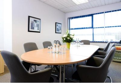 Professional meeting room with an oval wooden table and grey upholstered chairs.