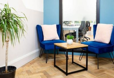 Small break area with two blue velvet armchairs and a wooden side table.