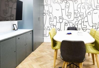 Meeting room with a white oval table, colorful chairs, and a creative face-patterned feature wall.