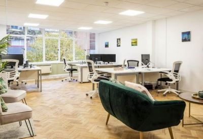 Lounge area with a dark green sofa, cream armchairs, and a coffee table in a bright workspace.