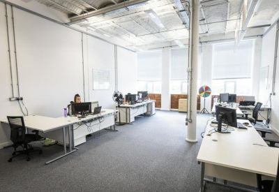 Open-plan office with white desks, ergonomic chairs, and large windows.