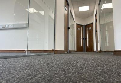 Perspective view of a carpeted office corridor with glass walls and wooden doors.