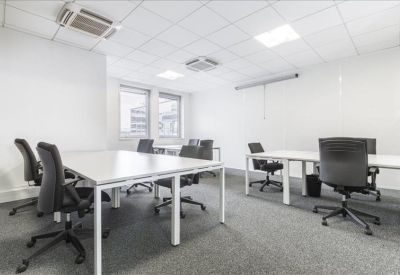 Spacious open-plan workspace with several white desks and ergonomic black chairs.