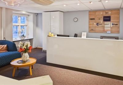 Brightly lit reception area with a long white desk and comfortable blue sofa.