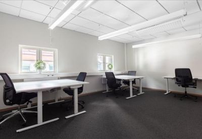 Spacious shared workspace with several white desks and ergonomic black chairs.