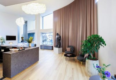 Bright reception lobby with a dark stone desk, wooden floors, and a tall curved curtain wall.