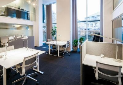 Open-plan coworking area with white desks, ergonomic chairs, and glass-walled mezzanine.