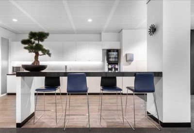 Sleek office kitchen and break area featuring a high breakfast bar with blue stools and a bonsai tree.