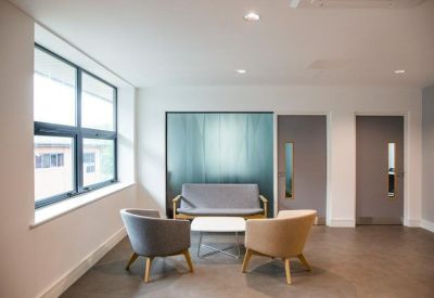 Bright lounge area with grey and tan armchairs and a decorative frosted glass partition.