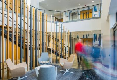 Double-height reception lobby featuring a staircase behind vertical wooden slats and lounge seating.