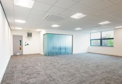 Spacious open-plan workspace with grey carpet tiles and a frosted glass room divider.