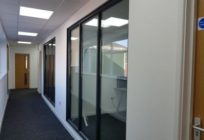 Bright office corridor with glass partitions and recessed ceiling lights.