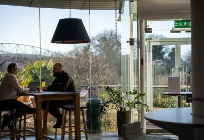 Bright glass-walled lounge with people at a high table and greenery.
