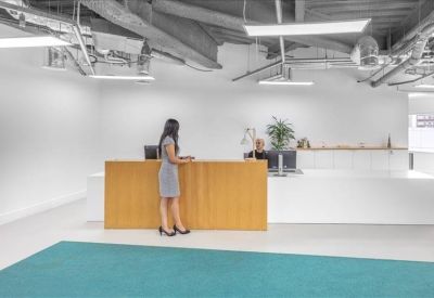 Bright reception area featuring a natural wood front desk and teal carpet runner.