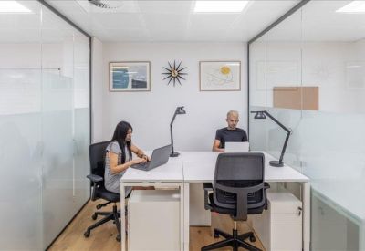 Small private office suite with glass partitions and two people working at white desks.