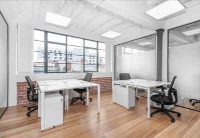 Bright office with white desks, black chairs, and large industrial windows.