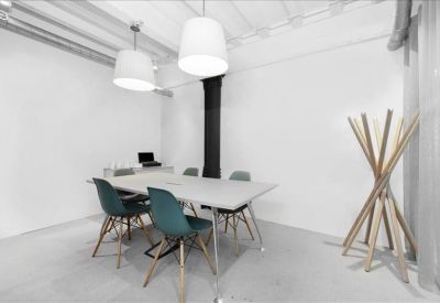 Minimalist meeting room with a white table, teal chairs, and a unique wooden coat rack.
