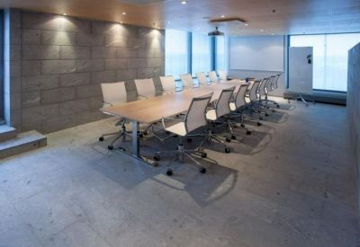 Professional meeting room with a long wooden table, white rolling chairs, and a grey stone wall.