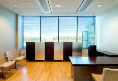 Bright private office suite featuring a dark wood desk, guest seating, and large windows.