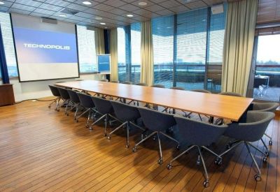 Professional boardroom with a long wooden table, grey ergonomic chairs, and a presentation screen.