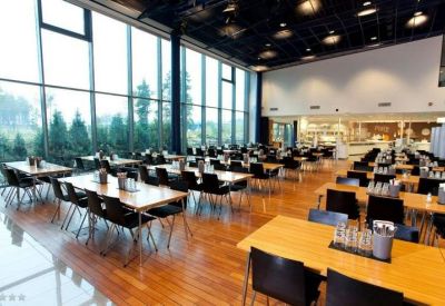 Spacious cafeteria with wooden tables, black chairs, and large floor-to-ceiling windows.